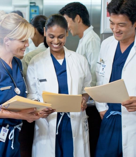 Three physicians standing together, looking down at paperwork while smiling