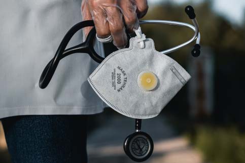 Healthcare worker standing outside and holding a mask and stethoscope 